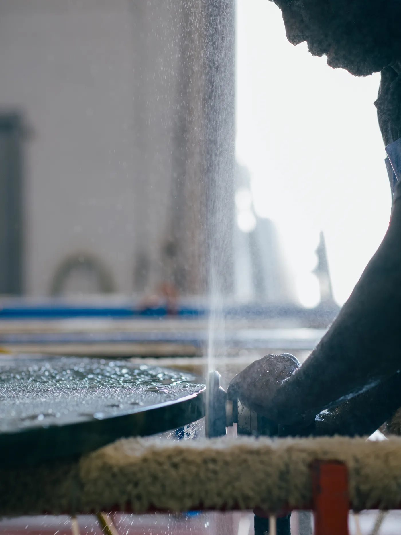 Fabricator hand-guiding a stone piece under running water
